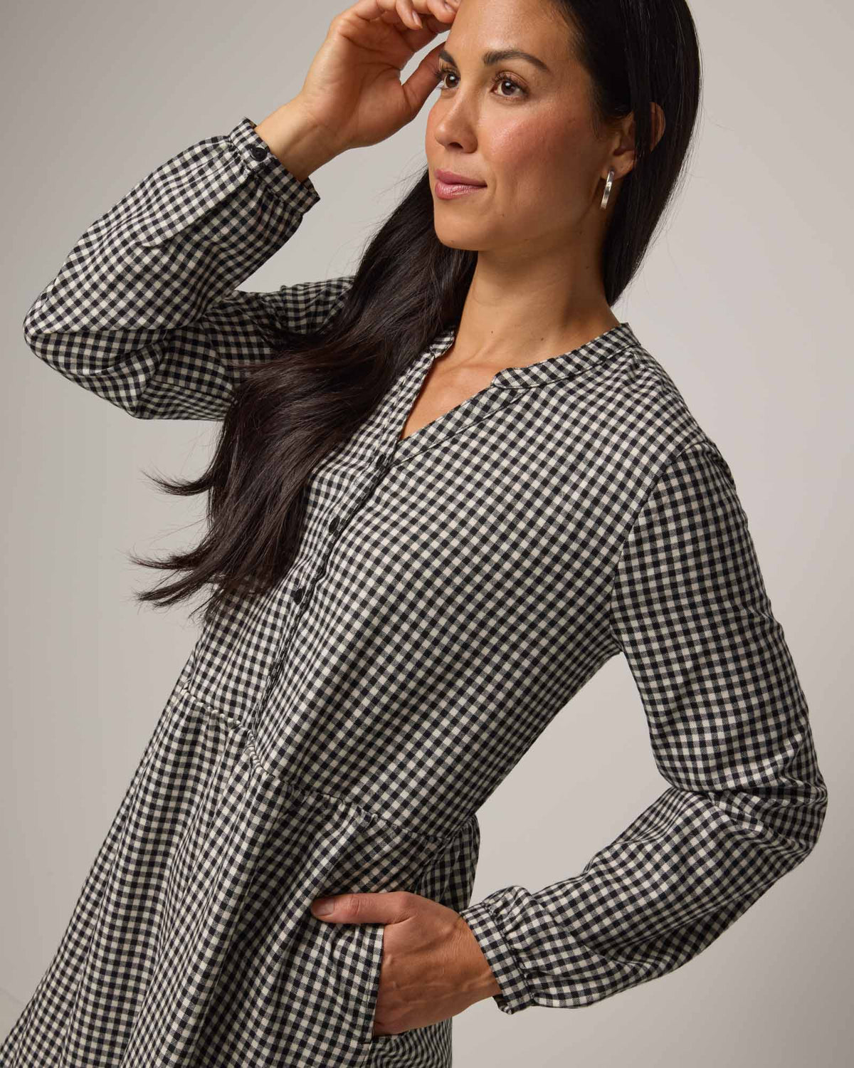 Model wearing Marika Brushed Twill Dress in Black & White Gingham. Marika Brushed Twill Dress is a merino wool long sleeve, gathered, midi swing dress with a button placket available in sizes XS-XXL.