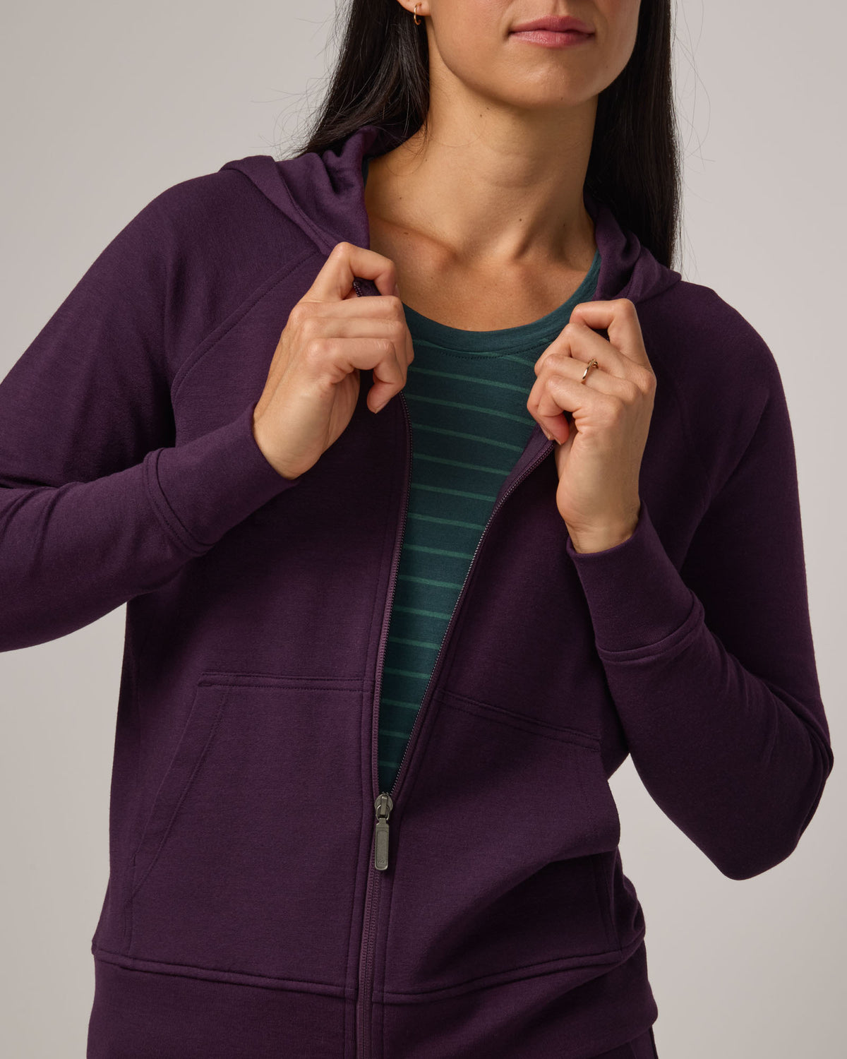 Model wearing Aspen Full-Zip Hoodie in Cassis, a deep purple color. Aspen Full-Zip Hoodie is a merino wool long sleeve zip hoodie with pockets available in sizes XS-3X.