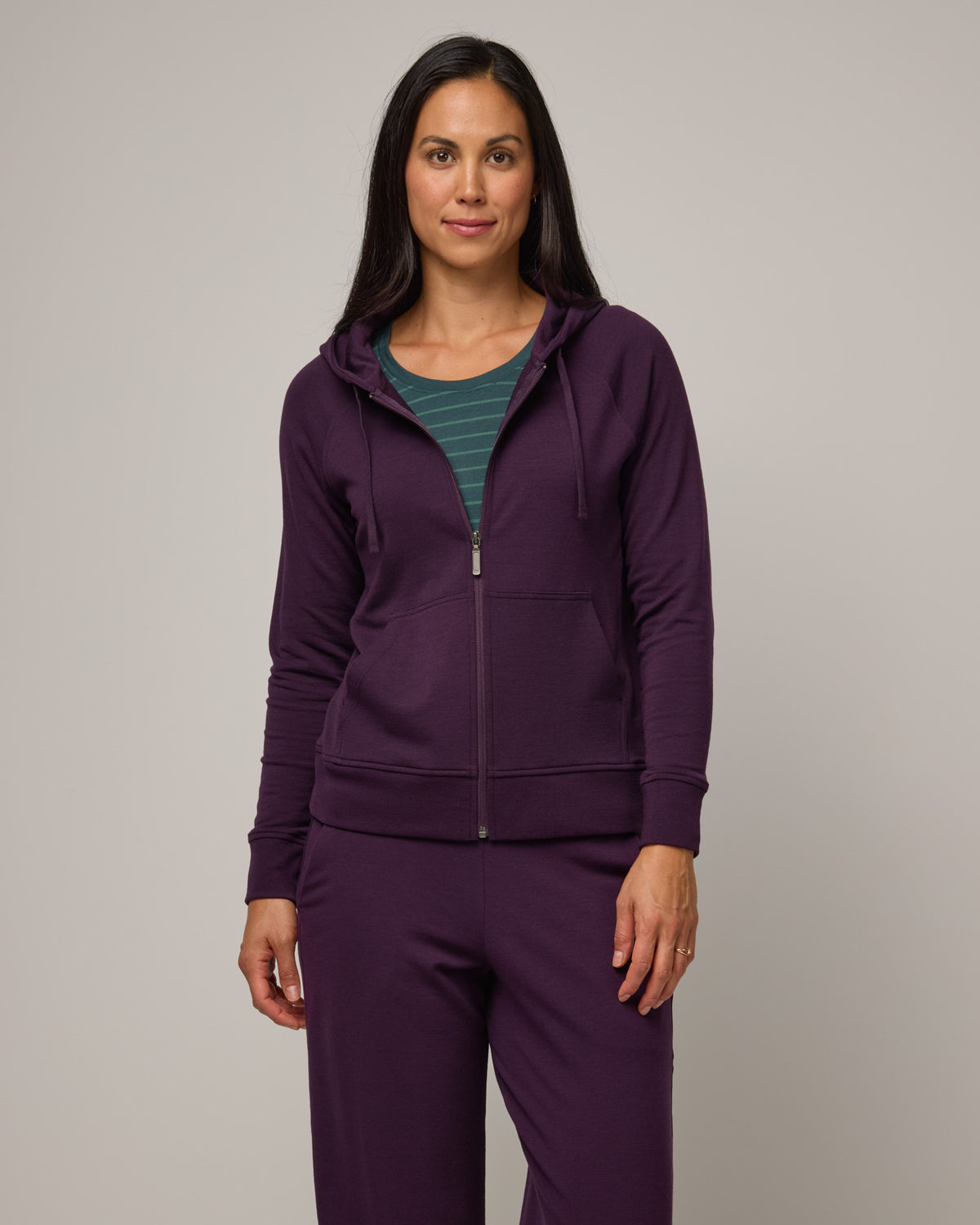 Model wearing Aspen Full-Zip Hoodie in Cassis, a deep purple color. Aspen Full-Zip Hoodie is a merino wool long sleeve zip hoodie with pockets available in sizes XS-3X.