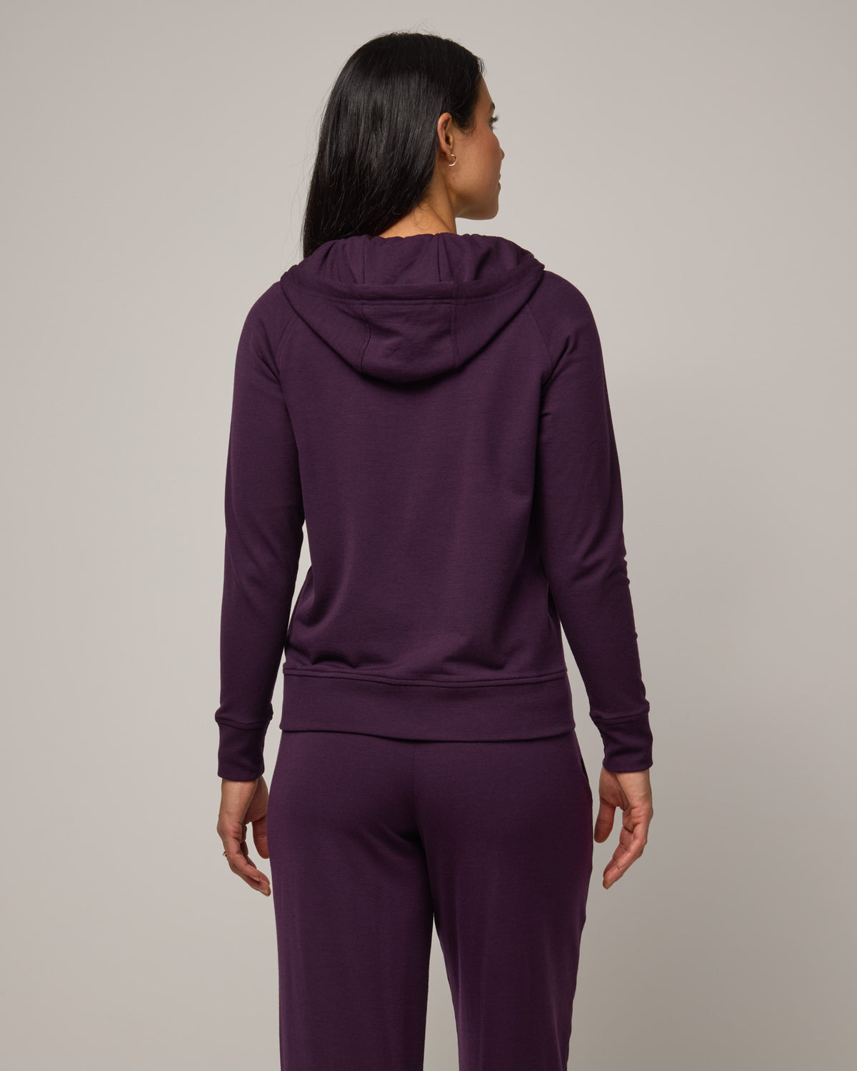 Model wearing Aspen Full-Zip Hoodie in Cassis, a deep purple color. Aspen Full-Zip Hoodie is a merino wool long sleeve zip hoodie with pockets available in sizes XS-3X.