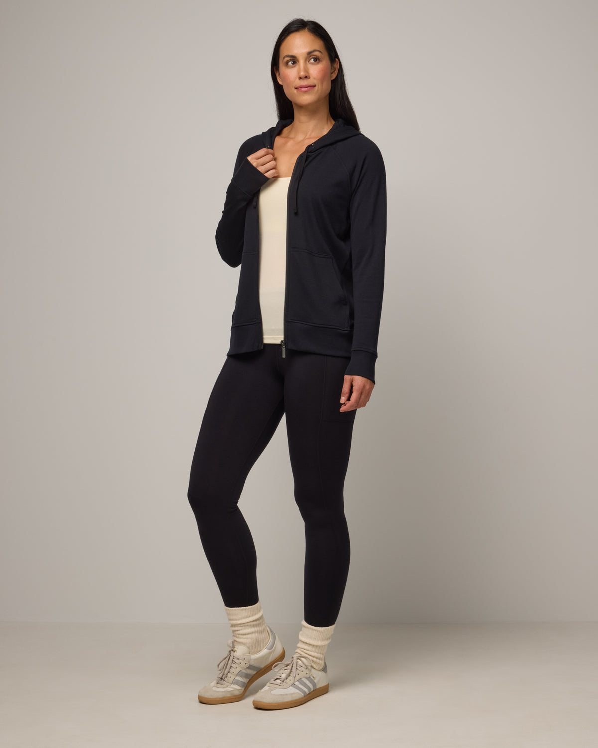 Model wearing Aspen Full-Zip Hoodie in Black. Aspen Full-Zip Hoodie is a merino wool long sleevezip hoodie with pockets available in sizes XS-3X.