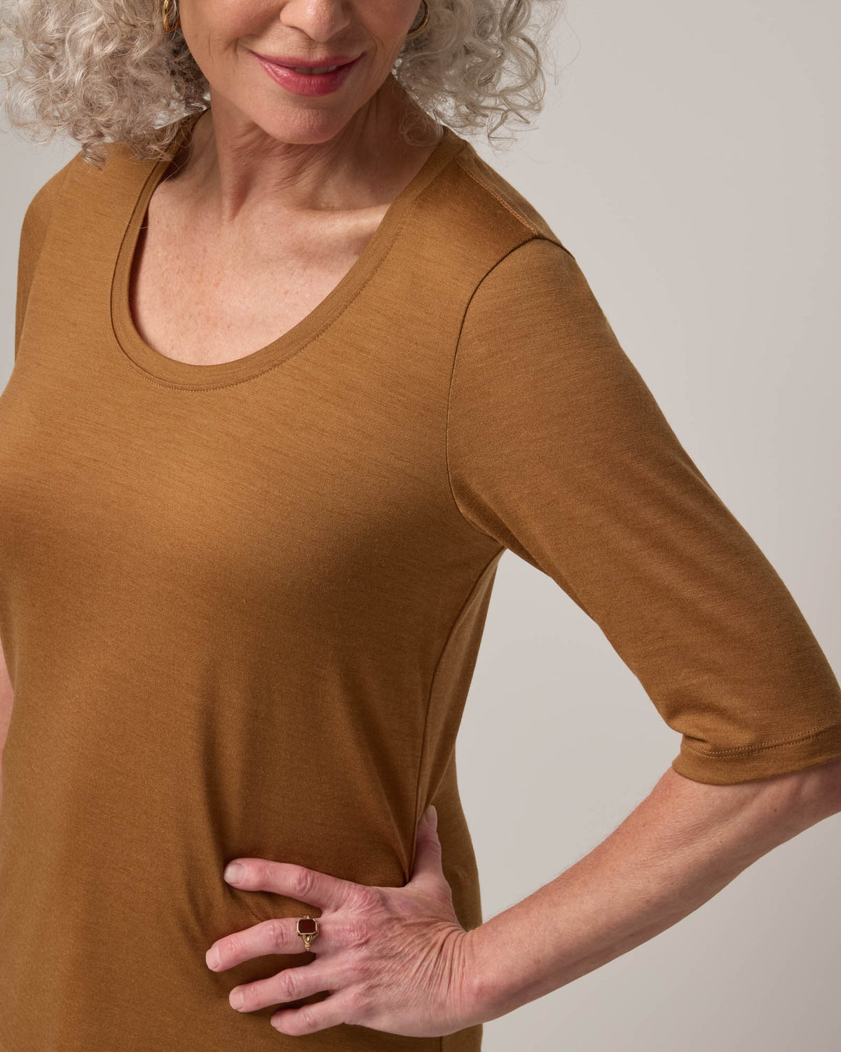 Model wearing Celine Signature Elbow-Sleeve Tee in Camel, a caramel brown color. Celine Signature Elbow Sleeve Tee is a merino wool scoop neck half-sleeve tee available in sizes XS-3X.