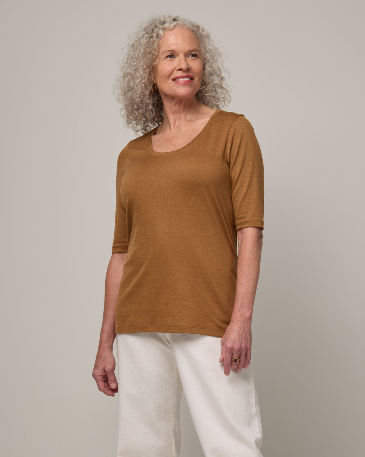 Model wearing Celine Signature Elbow-Sleeve Tee in Camel, a caramel brown color. Celine Signature Elbow Sleeve Tee is a merino wool scoop neck half-sleeve tee available in sizes XS-3X.