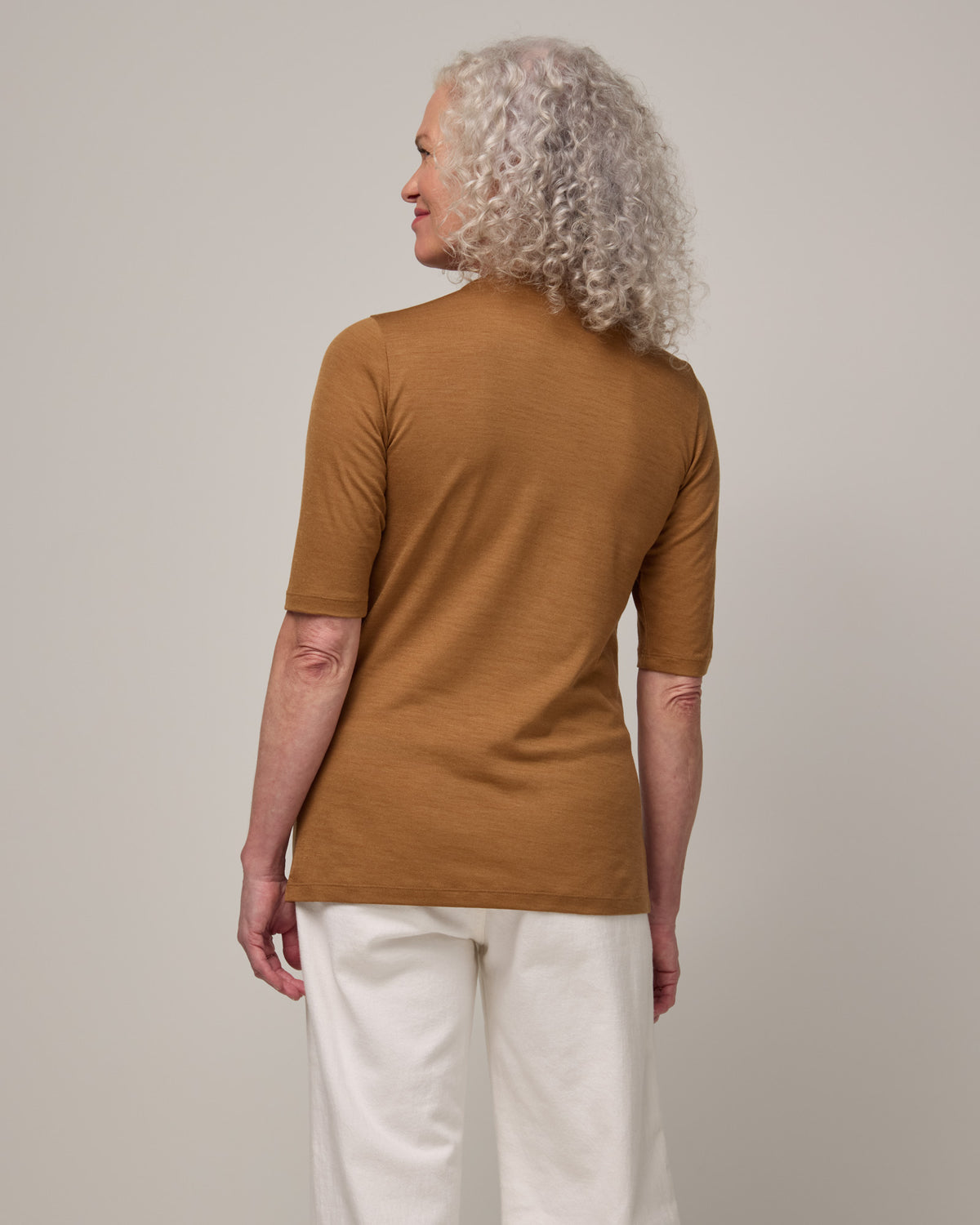 Model wearing Celine Signature Elbow-Sleeve Tee in Camel, a caramel brown color. Celine Signature Elbow Sleeve Tee is a merino wool scoop neck half-sleeve tee available in sizes XS-3X.