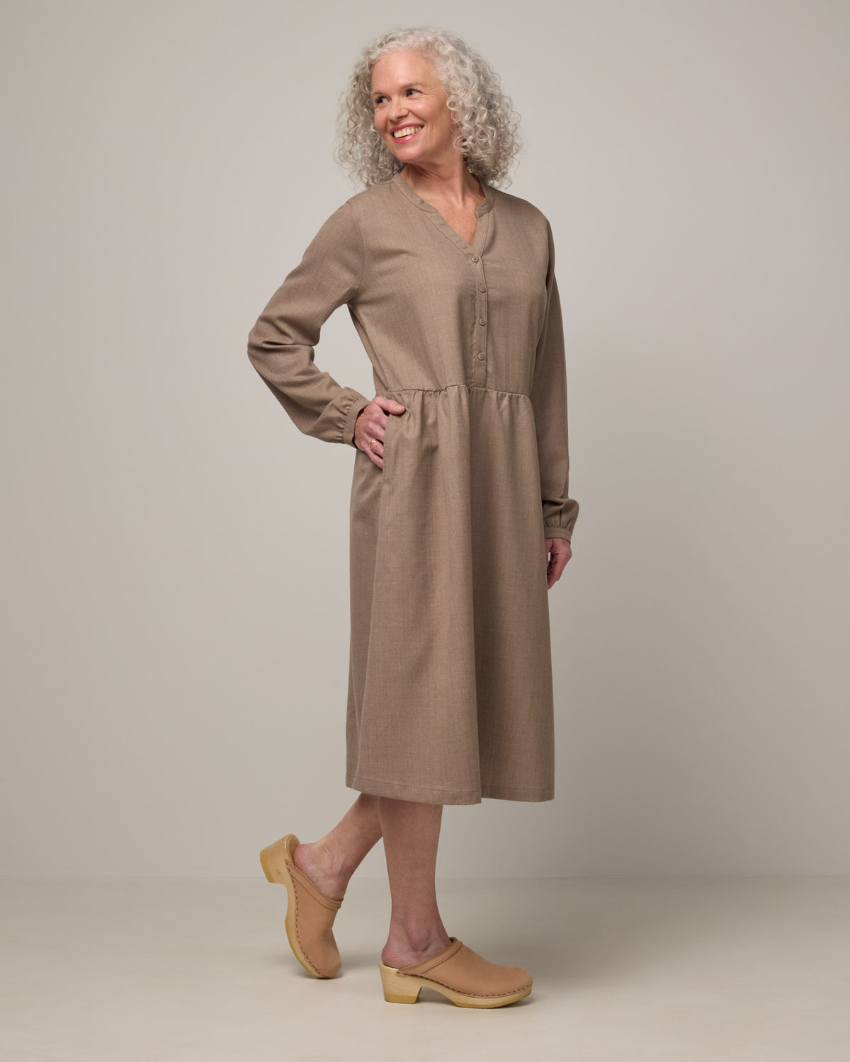 Model wearing Marika Brushed Twill Dress in Taupe heather, a heathered tan color. Marika Brushed Twill Dress is a merino wool long sleeve, gathered, midi swing dress with a button placket available in sizes XS-XXL.