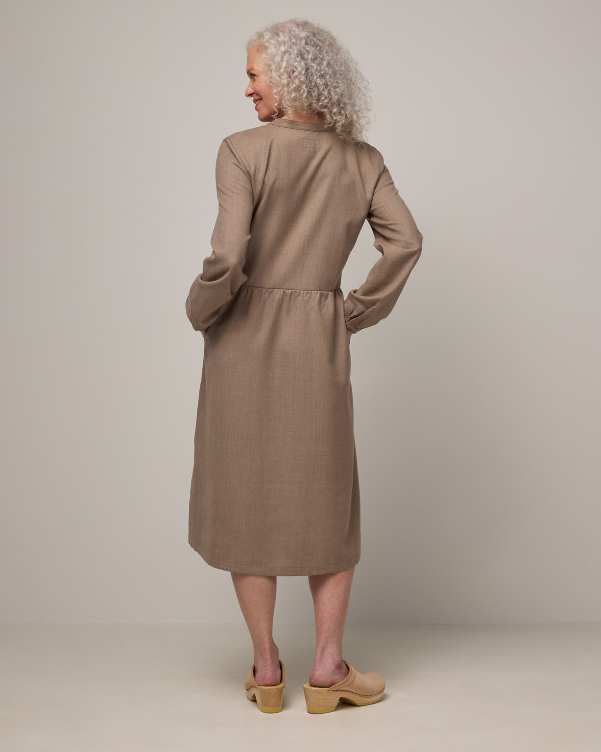 Model wearing Marika Brushed Twill Dress in Taupe heather, a heathered tan color. Marika Brushed Twill Dress is a merino wool long sleeve, gathered, midi swing dress with a button placket available in sizes XS-XXL.