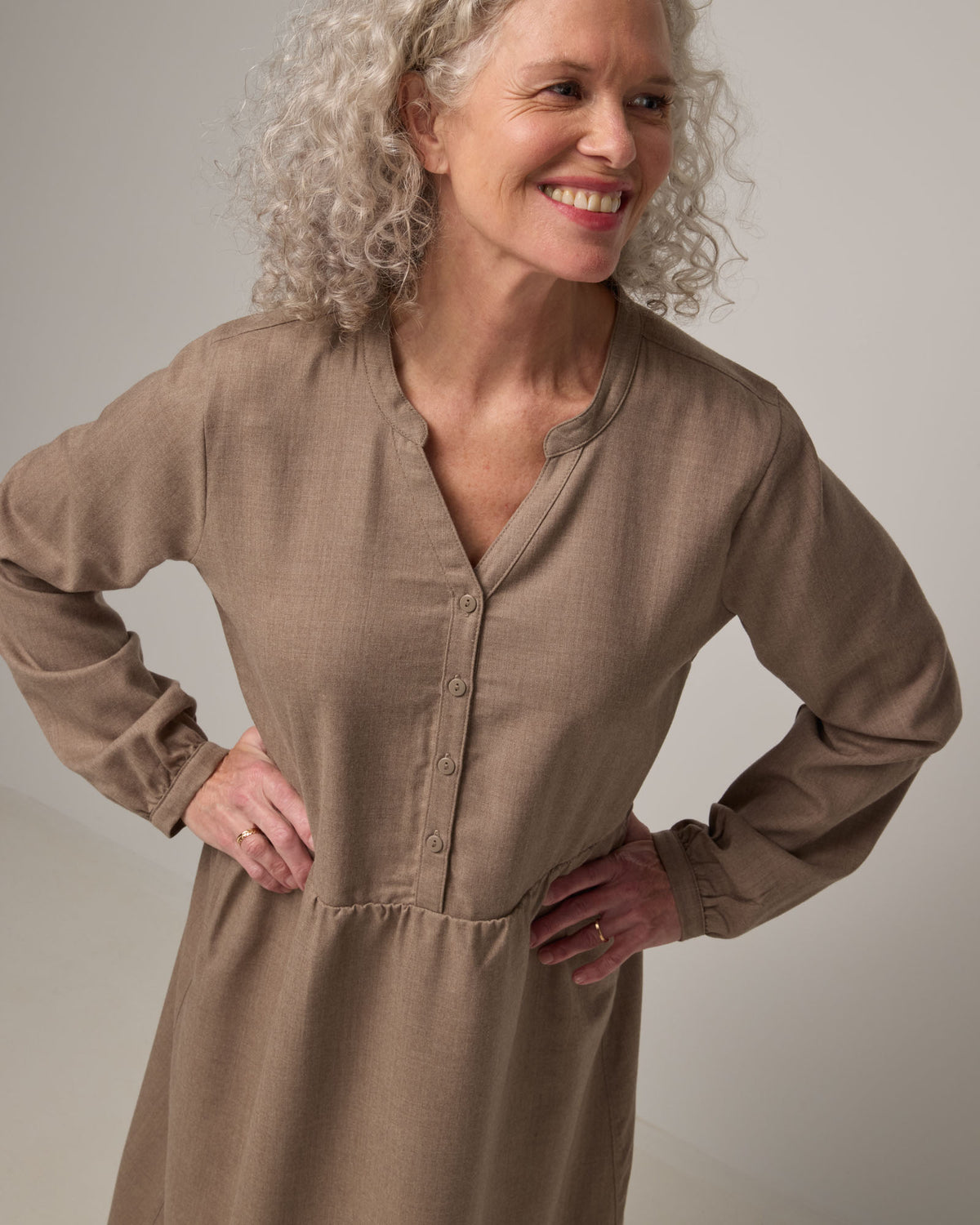 Model wearing Marika Brushed Twill Dress in Taupe heather, a heathered tan color. Marika Brushed Twill Dress is a merino wool long sleeve, gathered, midi swing dress with a button placket available in sizes XS-XXL.