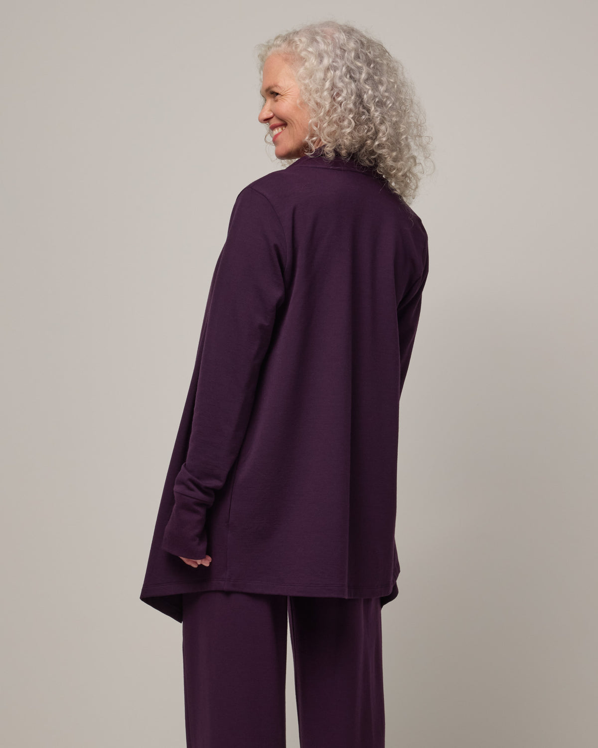 Model wearing Aspen Cardigan in Cassis, a dark purple color. Aspen Cardigan is a merino wool long sleeve cardigan with pockets available in sizes XS-3X.