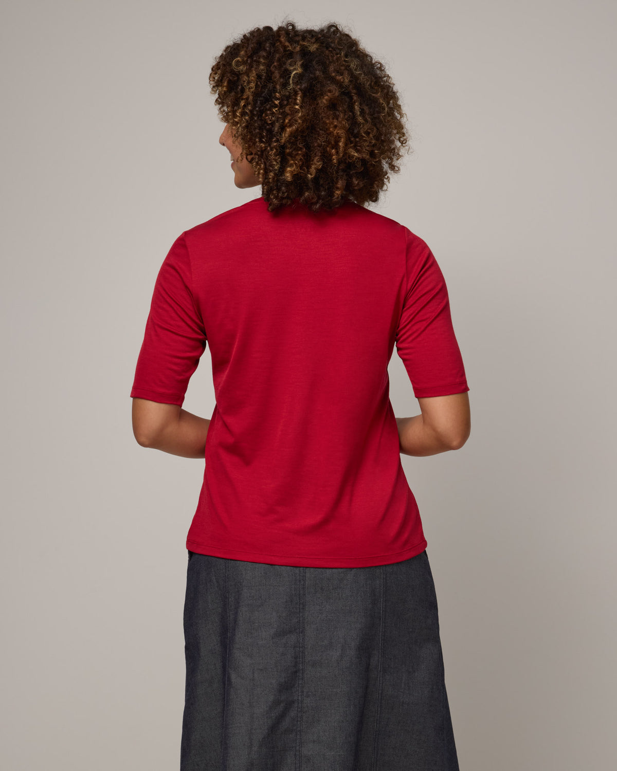 Model wearing Celine Signature Elbow-Sleeve Tee in Cherry Red, a bright red color. Celine Signature Elbow Sleeve Tee is a merino wool scoop neck half-sleeve tee available in sizes XS-3X. 