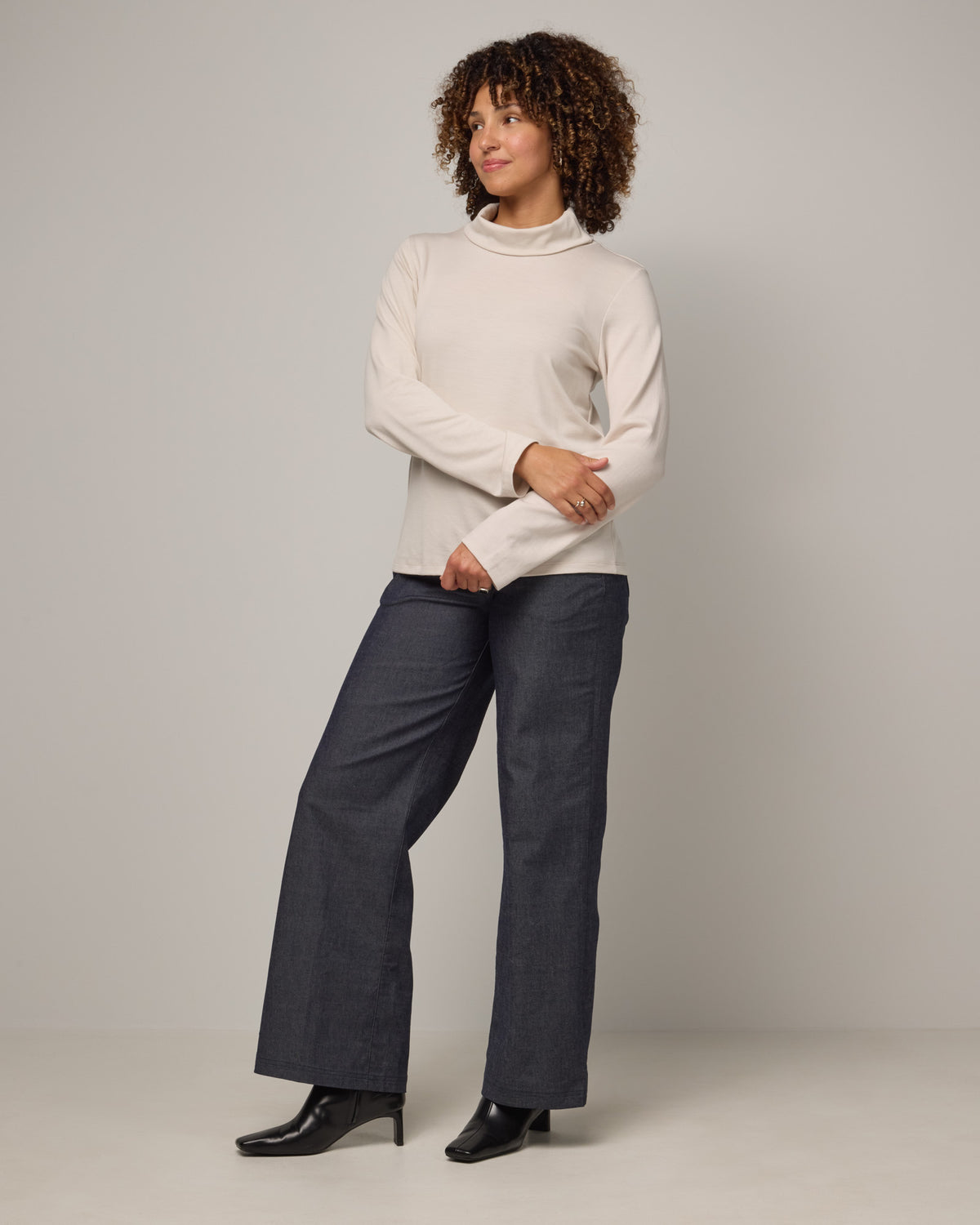 Model wearing Rylie Heavyweight Turtleneck Top in Oatmeal, a light cream color. Rylie Heavyweight Turtleneck Top is a merino wool long sleeve, relaxed fit turtleneck available in sizes XS-3X.