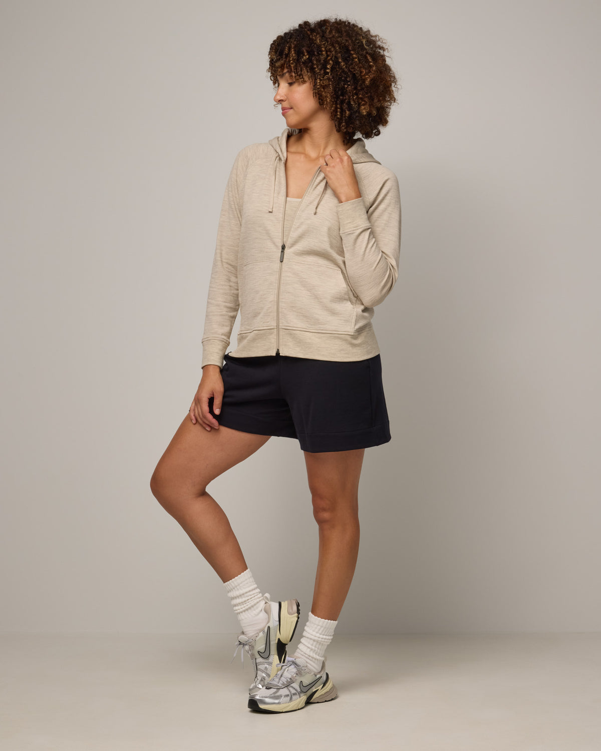 Model wearing Aspen Full-Zip Hoodie in Oatmeal Heather, a cream heather color. Aspen Full-Zip Hoodie is a merino wool long sleeve zip hoodie with pockets available in sizes XS-3X.