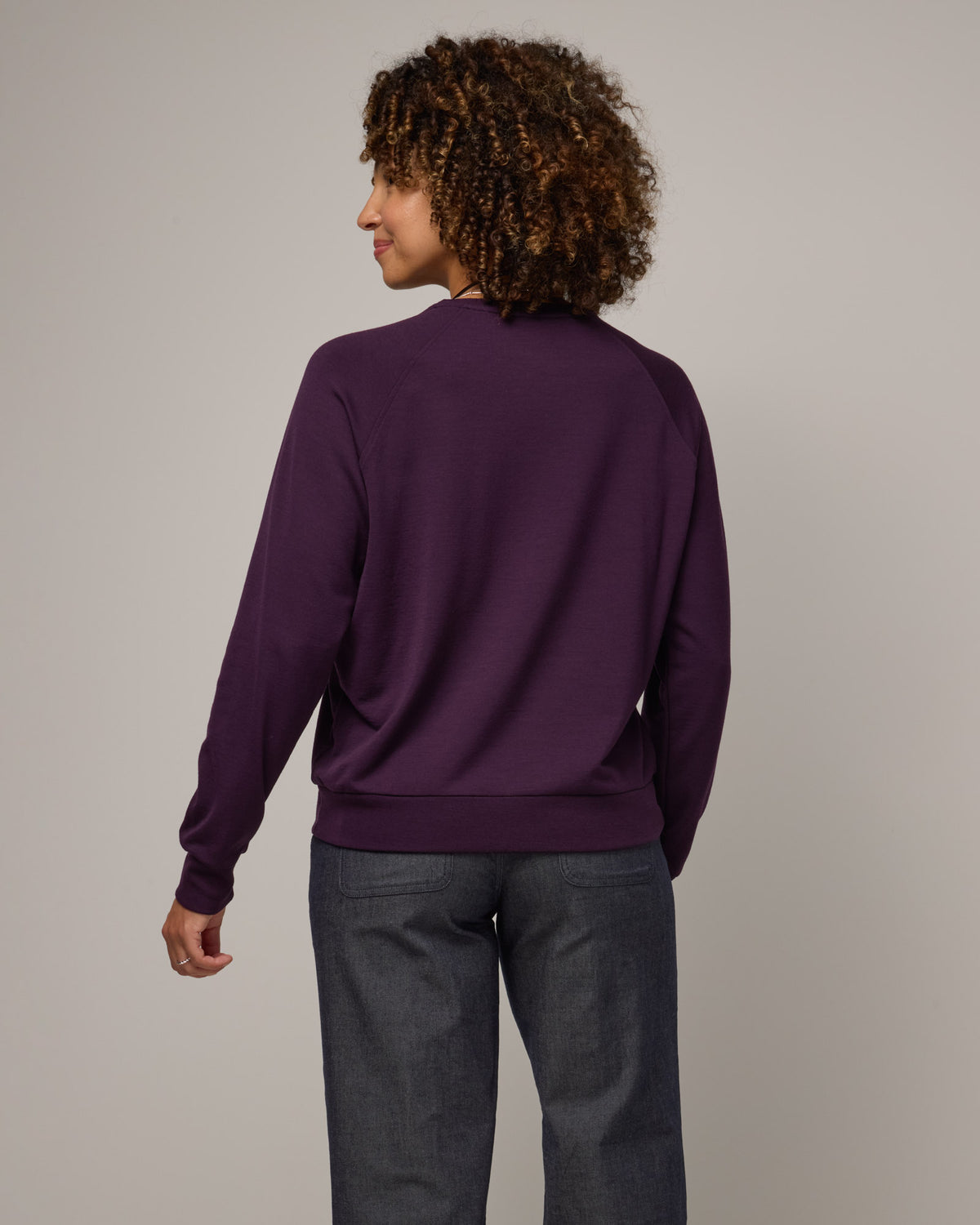 Model wearing Aspen Sweatshirt in Cassis, a dark purple color. Aspen Sweatshirt is a merino wool long sleeve, crew neck, regular fit sweatshirt available in sizes XS-3X.